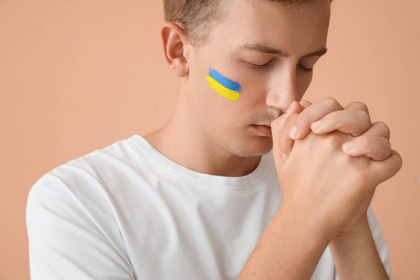 Jovem com bandeira hasteada da Ucrânia orando em fundo bege, close-up - Foto, Imagem
