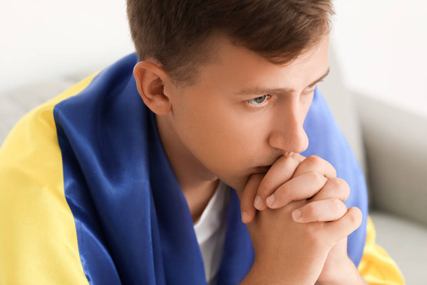 Молодой человек с флагом Украины молится дома, крупным планом - Фото, изображение