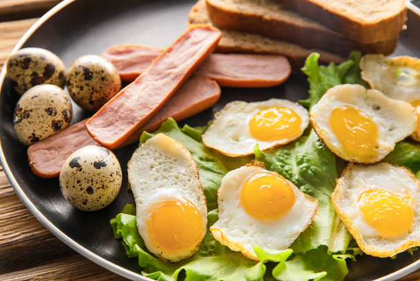 Сковородка с вкусными жареными перепелиными яйцами и сосисками, крупным планом - Фото, изображение