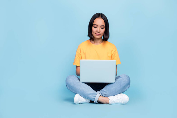 Full length photo of attractive young lady chinese focused manager student laptop wear trendy yellow look isolated on blue color background. - Φωτογραφία, εικόνα