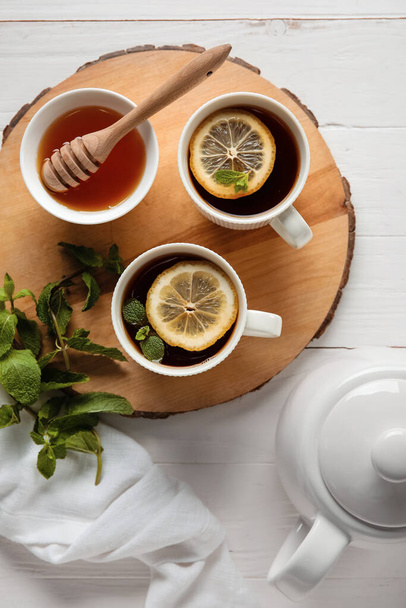 Levy kuppeja mustaa teetä, sitruunaa, minttua ja hunajaa valkoisella puupohjalla - Valokuva, kuva