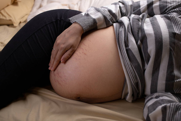 Pregnant woman touching her belly in the bed. Pregnancy, motherhood, and expectation - Fotoğraf, Görsel