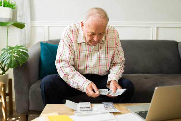 Onafhankelijke gelukkige oude man thuis tellen zijn pensioen geld en het doen van zijn maandelijkse financiën - Foto, afbeelding