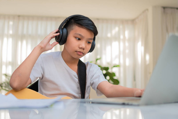 Azjatycki chłopiec gra na gitarze i ogląda kurs online na laptopie podczas ćwiczeń do nauki muzyki lub instrumentu muzycznego online w domu. Chłopiec studenci uczyć się online z wideo rozmowy nauczyciele grać na gitarze. - Zdjęcie, obraz