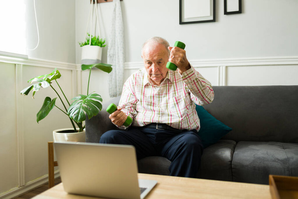 Активный пожилой человек, имеющий фитнес здоровый образ жизни упражнения с гантелями веса во время просмотра видео-учебник - Фото, изображение