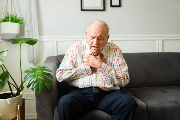 Homme âgé caucasien regardant malade tout en souffrant de problèmes cardiaques ou respiratoires et ayant une crise cardiaque seul à la maison - Photo, image