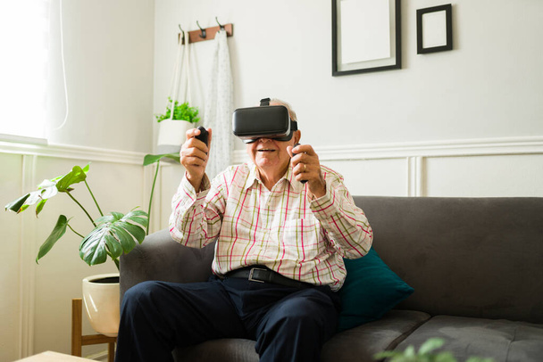 Cheerful elderly man playing videogames with virtual reality glasses and having fun with immersive technology - Photo, Image