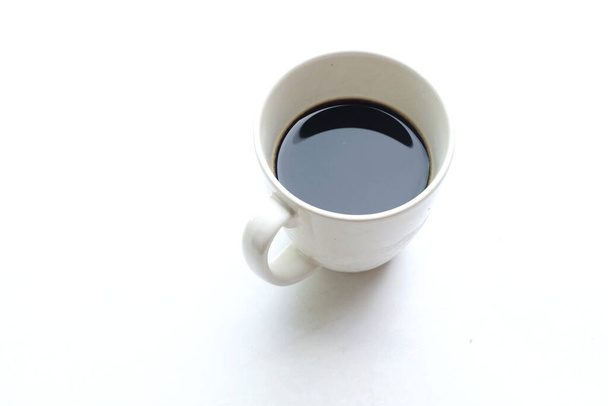 ένα καφέ ζεστό americano σε ένα ποτήρι λευκό φλιτζάνι το πρωί για να τους βοηθήσει να μείνουν ξύπνιοι και ανανεωμένοι, και έτοιμοι να εργαστούν απομονωμένοι σε ένα λευκό φόντο - Φωτογραφία, εικόνα