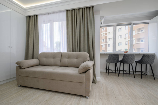 Μικρό στούντιο διαμέρισμα σαλόνι με καναπέ και τραπεζαρία με καρέκλες στο windowsill - Φωτογραφία, εικόνα