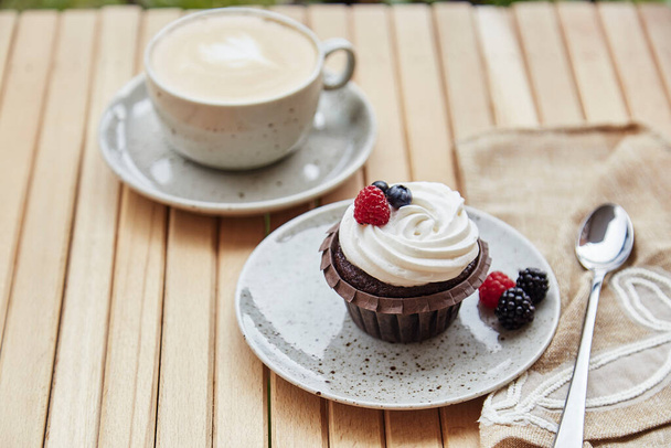 Creamy tender berries cupcake with cup of cappuccino outside. Atmospheric cozy lunch at the terrace. - Photo, Image