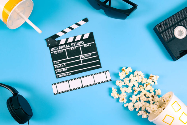 Movie clapperboard, popcorn, film strip, retro videotape, headphones and paper glass with drink on blue background, top view close-up. Cinema concept. - Φωτογραφία, εικόνα