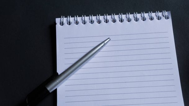 Horní pohled na zápisník s perem na černém stole. notepad s prostorem pro kopírování pera a textovým prostorem - Fotografie, Obrázek