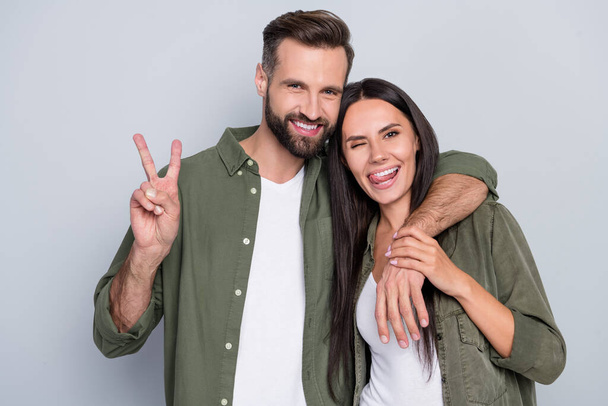 Portrait of handsome beautiful trendy cheerful couple cuddling showing v-sign isolated over grey pastel color background. - Foto, imagen