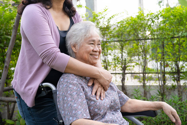 Pflegetochter hilft asiatischer Seniorin im Elektro-Rollstuhl im Park. - Foto, Bild