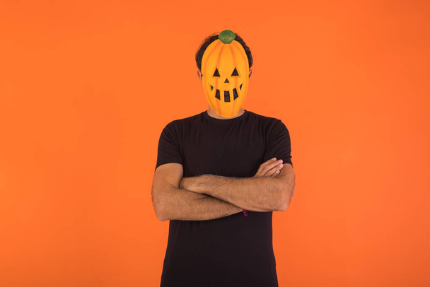Person mit Kürbismaske, die mit verschränkten Armen auf orangefarbenem Hintergrund Halloween feiert. Konzept der Feier, Allerseelen und Allerheiligen. - Foto, Bild