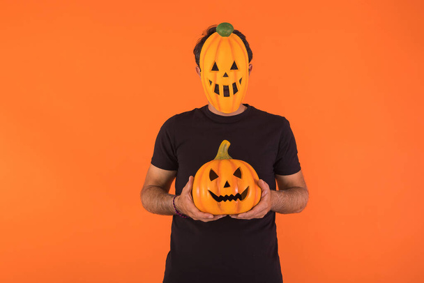 Persona con máscara de calabaza celebrando Halloween, sosteniendo una calabaza, sobre fondo naranja. Concepto de celebración, Día de Todas las Almas y Día de Todos los Santos. - Foto, Imagen