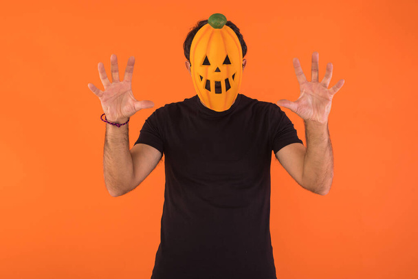 Persona con máscara de calabaza celebrando Halloween, asustando, sobre fondo naranja. Concepto de celebración, Día de Todas las Almas y Día de Todos los Santos. - Foto, imagen