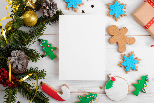 Vánoční 5x7 karta mokup šablona s vánoční perník sušenky, přírodní jedle větvičky a slavnostní výzdoba na bílém dřevěném pozadí, nahoře, byt ležel, kopírovací prostor - Fotografie, Obrázek