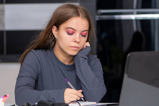 Nuori tyttö kirjoittaa kannettavan tietokoneen ääressä olevaan muistikirjaan. Konsepti: etäopetus, vieraiden kielten oppiminen, itseopiskelu. - Valokuva, kuva