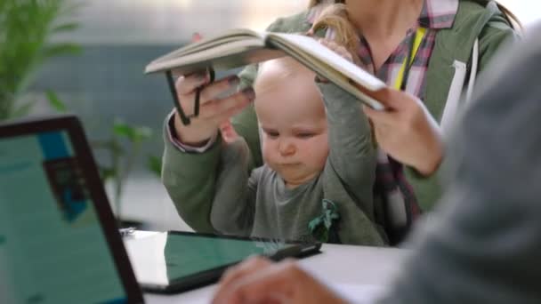 Mother with baby, businesswoman with notebook and communication with worker in office at desk. Motherhood, inclusion and female with kid working with tablet, notes or book after maternity leave - Footage, Video
