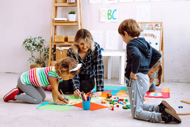 Female psychiatrist, pedagogue playing and learning to imagine with children, creative painting in mental health development center for preschoolers. Attention deficit disorder, children autism - Photo, Image