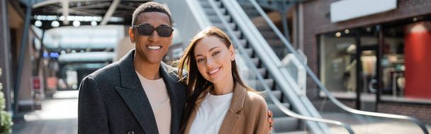 african american man in sunglasses and young stylish woman looking at camera on urban street, banner - Фото, зображення