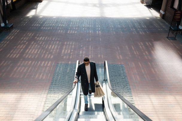 high angle view of fashionable african american man with shopping bags on escalator - Fotó, kép