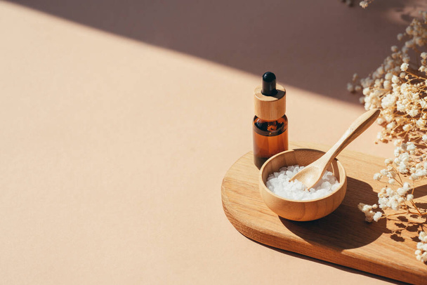 Amber dropper bottle with serum, tonic or essential oil and bowls filled with white bath sea salt on wooden tray. Beauty concept for face and body care. Natural cosmetic and dry flowers - 写真・画像