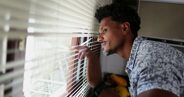 Чорний чоловік дивиться через кухонні жалюзі, дивлячись на вулицю
 - Фото, зображення