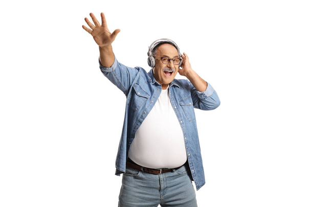 Happy mature man in a denim shirt listening to music and dancing isolated on white background - Zdjęcie, obraz