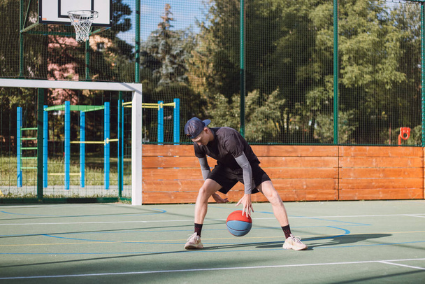 Young talent practices dribbling the basketball under his feet and improves his hand, body and foot coordination. Basketball game. Learning the trick, the deception. - Фото, изображение