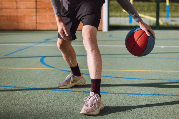 Νεαρό ταλέντο εξασκεί dribbling το μπάσκετ κάτω από τα πόδια του και βελτιώνει το χέρι, το σώμα και το πόδι του συντονισμού. Παιχνίδι μπάσκετ. Μαθαίνοντας το κόλπο, την εξαπάτηση. - Φωτογραφία, εικόνα