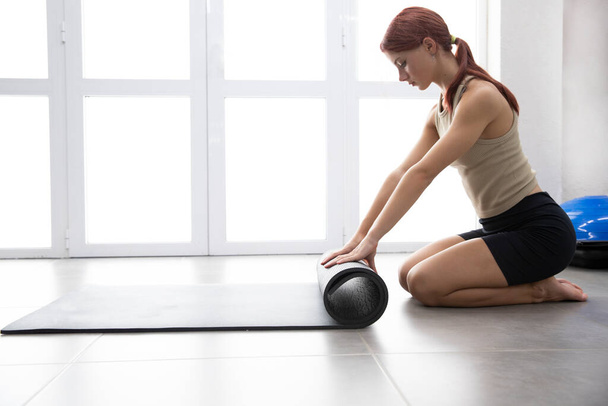 Sexy mooie sportvrouw meisje rolt een fitness mat. Plaats voor tekst. Yoga! Turnen - Foto, afbeelding