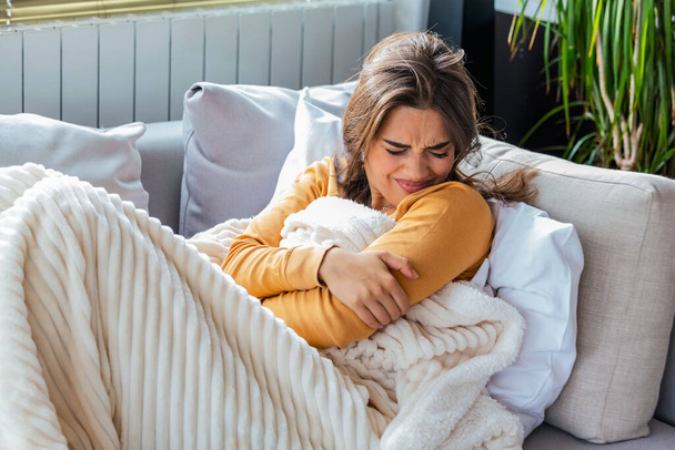Femme dans l'expression douloureuse tenant la main contre le ventre souffrant de douleurs menstruelles, couché triste sur le lit à la maison, ayant des crampes d'estomac dans le concept de santé féminine - Photo, image