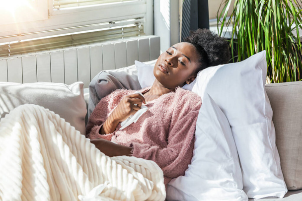 Sickness, seasonal virus problem concept. Woman being sick having flu lying on sofa looking at temperature on thermometer. Sick woman lying in bed with high fever. Cold flu and migraine. - Foto, afbeelding