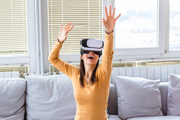 Mosolyogj boldog nő szerzés tapasztalat segítségével VR-headset szemüveg virtuális valóság otthon. Boldog meghökkent fiatal nő virtuális valóság headset vagy 3D-s szemüveg ül kanapén otthon - Fotó, kép