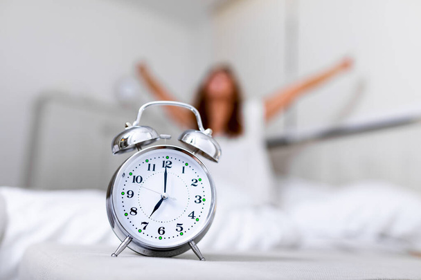 Будильник с будильником, счастливая женщина, лежащая в постели после пробуждения, солнечный свет утром. Проснуться утром вовремя. - Фото, изображение