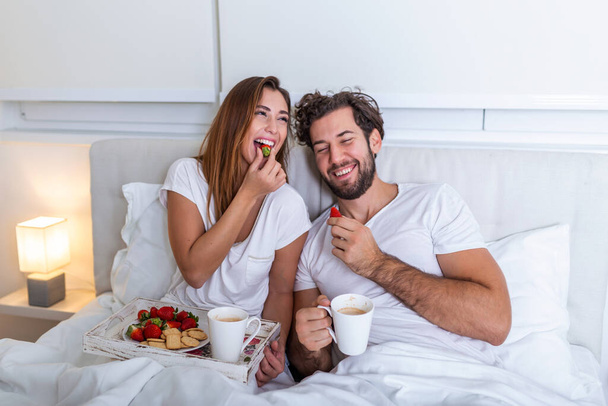 Mladý zamilovaný manželský pár jedl snídani ve své posteli. Dobré ráno! Zdravá snídaně v posteli. Mladý krásný milostný pár snídá v posteli. - Fotografie, Obrázek