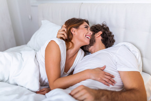 美しい愛情のカップルベッドでキス。美しい若いカップルがベッドの上に横になって。ロマンチックな若いカップルの愛のベッドの上に横たわる。美しいカップル笑顔でベッド. - 写真・画像