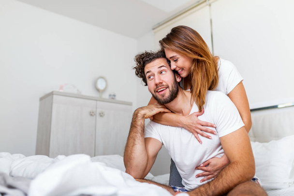 ベッドでパートナーを受け入れる女性、感情や愛を示すベッドで幸せなカップル。美しい愛情のカップルベッドでキス。美しい若いカップルがベッドの上に横になり. - 写真・画像