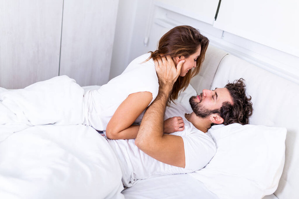 美しい愛情のカップルベッドでキス。美しい若いカップルがベッドの上に横になって。ロマンチックな若いカップルの愛のベッドの上に横たわる。美しいカップル笑顔でベッド. - 写真・画像