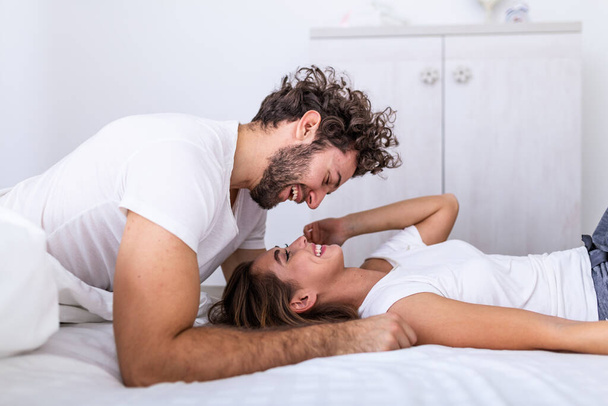Affectueux jeune couple attrayant partageant un moment romantique dans la chambre à coucher à la maison. Heureux jeune couple étreignant et souriant tout en étant couché sur le lit dans une chambre à coucher à la maison. - Photo, image