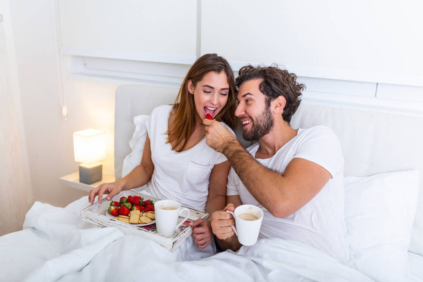 Verliebtes Paar frühstückt im Bett. Junges kaukasisches Paar beim romantischen Frühstück im Bett. Weibchen und Männchen, zwei Tassen Kaffee, Früchte und bunte Kekse. - Foto, Bild