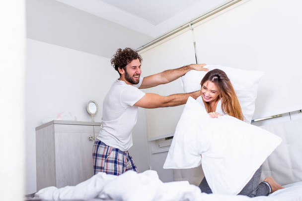 Happy young couple is having fun in bed. Enjoying the company of each other. Pillow battle Funny couple fighting with pillows in bed - 写真・画像