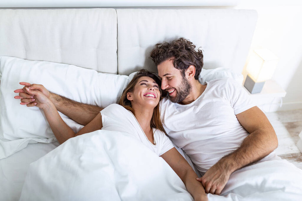 Νεαρό ερωτευμένο ζευγάρι στο κρεβάτι. Νεαρό ζευγάρι ξαπλωμένο στο κρεβάτι και γελώντας γαργαλώντας ο ένας τον άλλον. Ευτυχισμένο αισθησιακό νεαρό ζευγάρι ξαπλωμένο στο κρεβάτι μαζί το πρωί - Φωτογραφία, εικόνα
