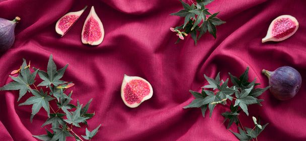 Fresh halved fig fruits and green maple leaves on raspberry red silk textile background. Panoramic banner image. Vibrant magenta and raspberry red Autumntime colors. - Zdjęcie, obraz