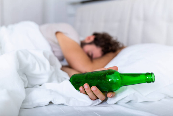 Po piciu. Pijany brodaty dorosły mężczyzna leżący na łóżku i śpiący po wypiciu dużej ilości alkoholu, pusta butelka na łóżku, alkoholizm, uzależnienie od alkoholu i koncepcja ludzi - Zdjęcie, obraz
