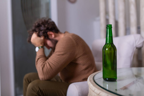 Depressiver trauriger junger süchtiger Mann, der sich schlecht fühlt, wenn er allein zu Hause Bier trinkt, gestresster frustrierter einsamer Trinker Alkoholiker, der unter Alkoholabhängigkeit leidet und ein Alkoholproblem hat, Alkoholismus-Konzept - Foto, Bild