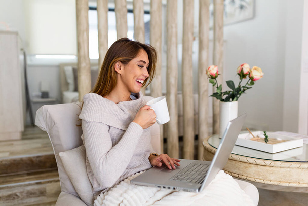Szczęśliwy uśmiechający się kobieta siedzi na kanapie, kanapa i korzysta z laptopa w living pokój w domu, oglądając film zabawny, Nauka języka, wideorozmowy, matka pracuje w trybie online - Zdjęcie, obraz