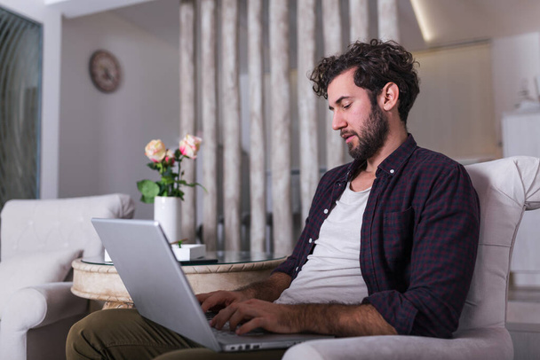 Man using laptop computer, working at home. Worried about finances. Handsome man with beard working at home on project, he is sitting on sofa looking at his laptop in front of him. work from home - Photo, Image